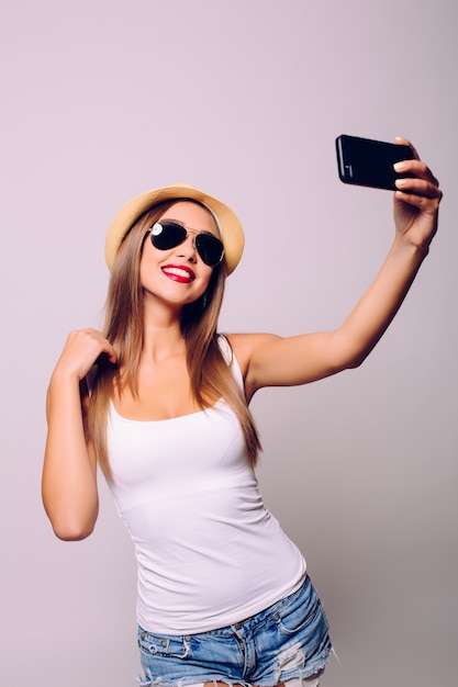 Portrait of a cheerful woman making selfie photo over gray wall