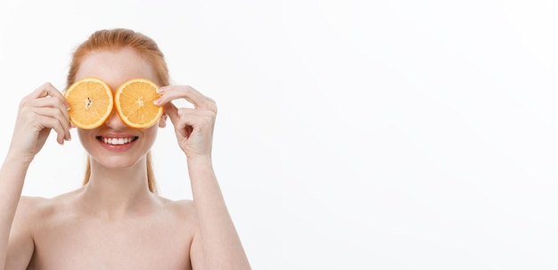 Free photo portrait of a cheerful young girl holding two slices of an orange at her face over white wall backgr