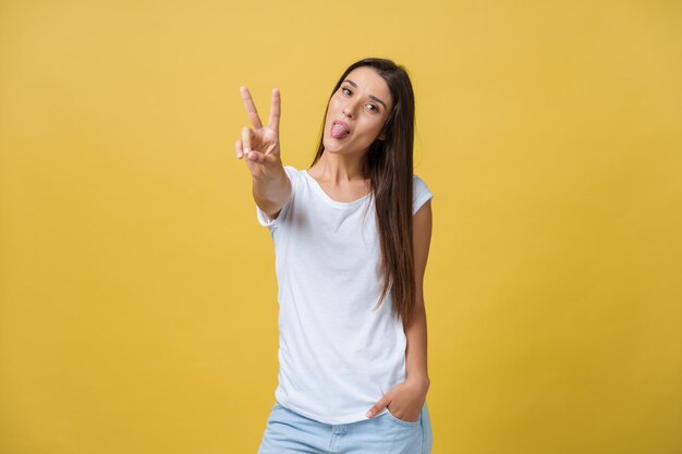 Portrait of cheerful young woman showing two fingers or victory gesture over yellow background