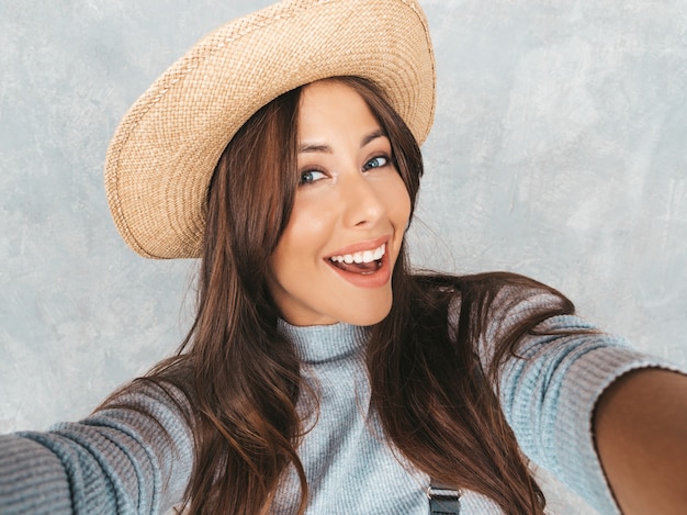 Portrait of cheerful young woman taking photo selfie and wearing modern clothes and hat.  