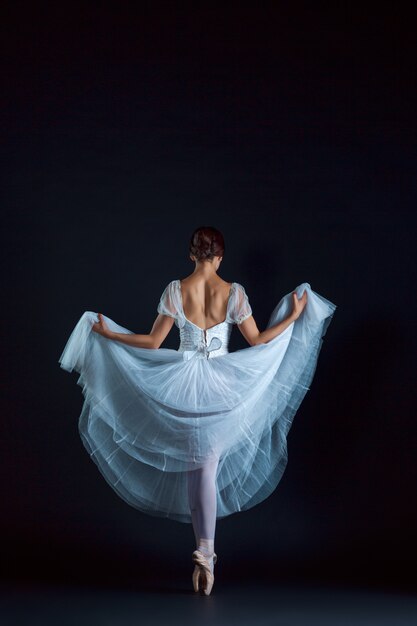 Portrait of the classical ballerina in white dress on black wall