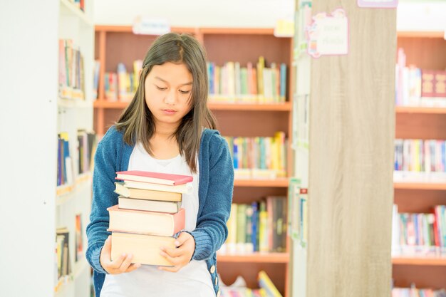 Portrait of clever student with open book reading it in college library