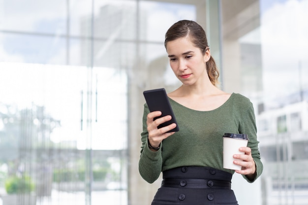 Portrait of concentrated young woman reading message on phone