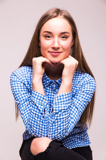 Portrait of a confident blond woman with hand on chin sitting at table against a white wall