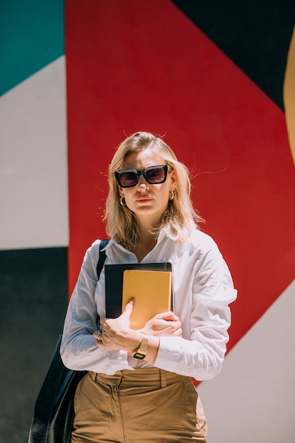 Portrait of a confident blonde young businesswoman standing against colored painted wall