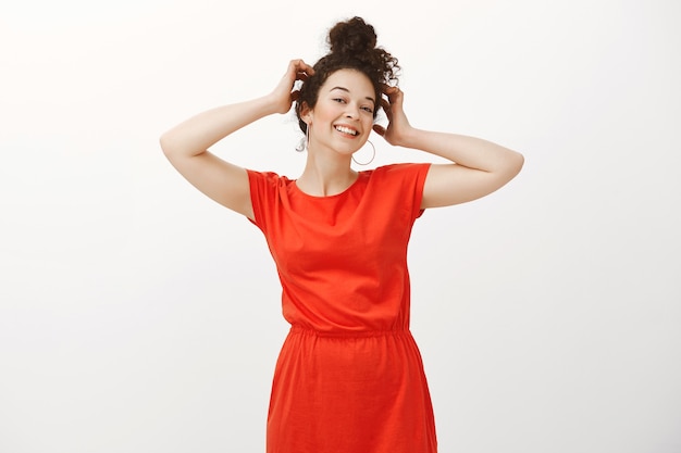 Portrait of confident carefree european female with combed curly hair, holding hands on head and smiling positively