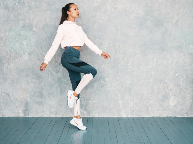 Portrait of confident fitness woman in sports clothing looking confident.Female jumping in studio near gray wall