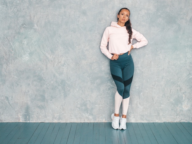 Portrait of confident fitness woman in sports clothing looking confident.Female posing in studio near gray wall