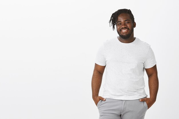 Portrait of confident guy with braids posing against the white wall