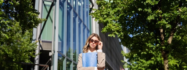 Free photo portrait of confident office lady business woman in sunglasses posing outdoors near her company