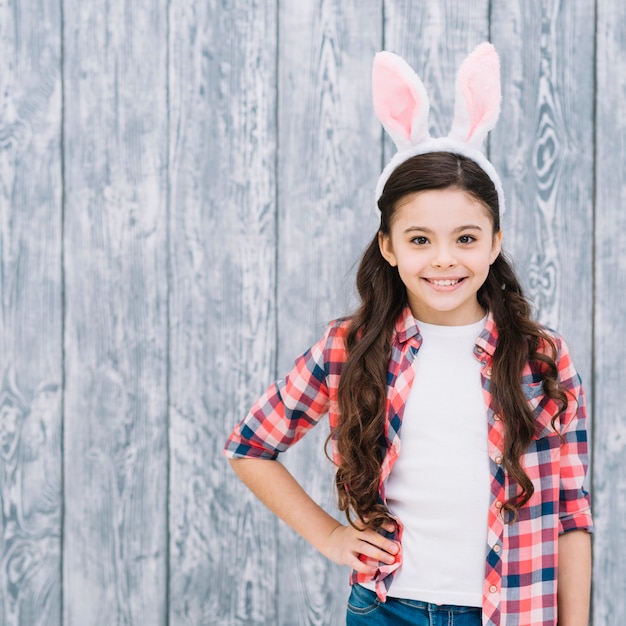 Free photo portrait of a confident smiling girl with bunny ear on head against wooden backdrop