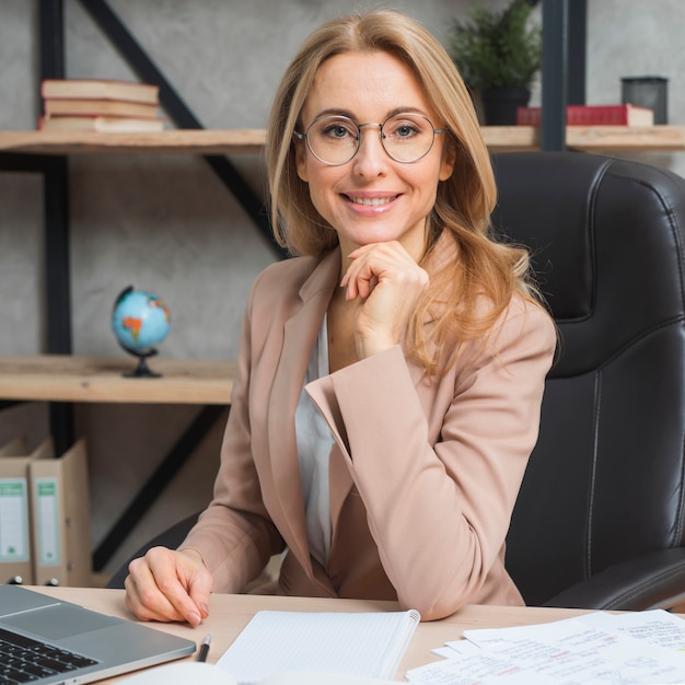 Portrait of a confident young blonde businesswoman sitting on chair at workplace