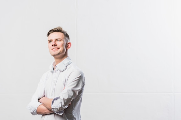 Free photo portrait of confident young man with headphone around his neck standing with his arms crossed against white wall