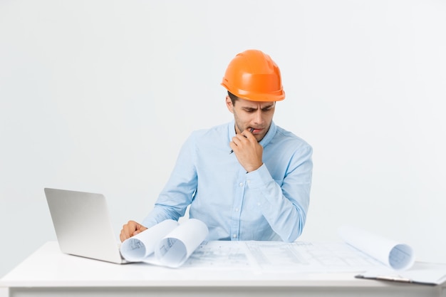 Free photo portrait of confused male designer or architect, feels stressed, being nervous, keeps hand on head, stares in blueprint. exhausted man creates construction project alone, has some troubles.