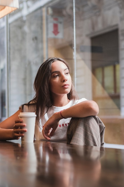 Portrait of a contemplated young woman holding disposable coffee cup in hand looking away