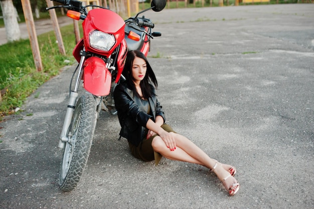 Portrait of a cool and awesome woman in black leather jacket sitting by a cool red bike