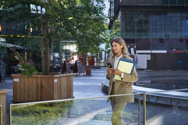 Free photo portrait of corporate woman in suit using mobile phone waiting for business partner in city center h