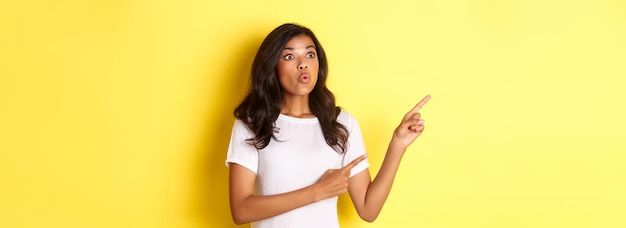 Portrait of cute africanamerican girl looking curious and pointing fingers at upper left corner foun