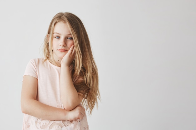 Free photo portrait of cute blonde little girl in pink t-shirt holding head with hand, being tired and bored during school classes.copy space