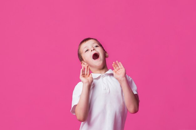 Portrait of cute boy screaming with mouth open on pink backdrop