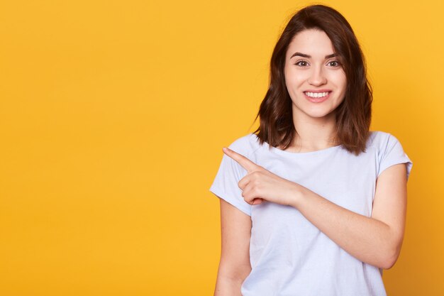 Portrait of cute charming cheerful girl pointing aside with index finger