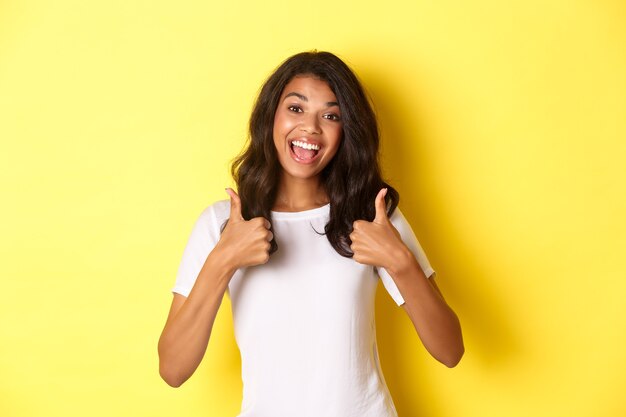 Portrait of cute and cheerful africanamerican girl showing thumbsup in support like and agree