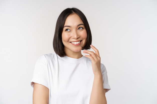 Portrait of cute coquettish woman laughing and smiling looking aside thoughtful thinking or imaging smth standing in white tshirt over studio background