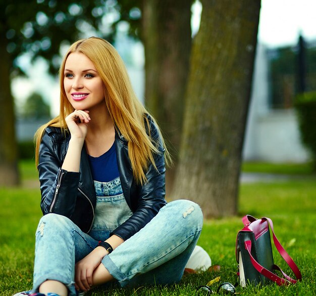 portrait of cute funny blond modern sexy urban young stylish smiling woman girl model in bright modern cloth outdoors sitting in the park in jeans with pink bag