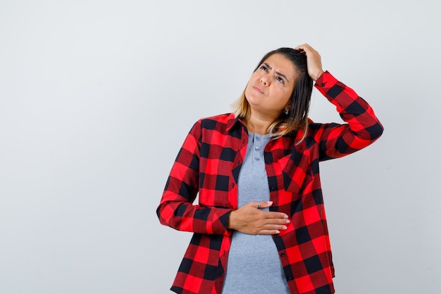 Portrait of cute lady keeping hand on head, looking up in casual clothes and looking pensive front view