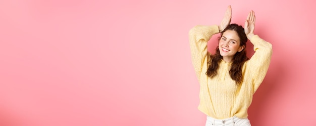 Free photo portrait of cute lady showing easter bunny ears gesture and smiling posing like silly rabbit standin