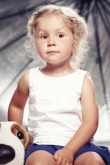 Free photo portrait of a cute little girl in casual dress sitting with a plush toy in a studio.