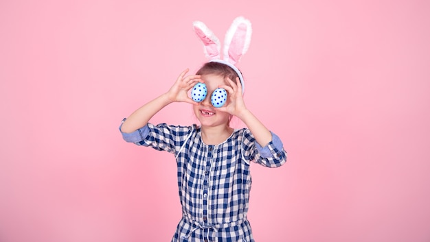 Free photo portrait of a cute little girl with easter eggs on a pink background.