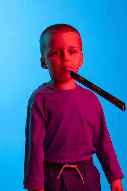 Free photo portrait of cute looking baby boy posing isolated over blue background in neon light