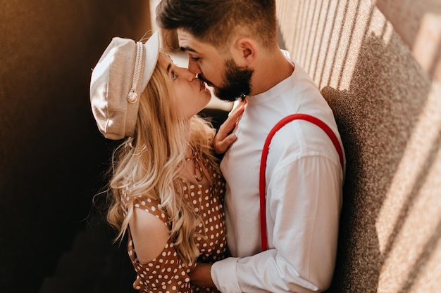 Free photo portrait of cute romantic couple kissing outdoors on sunny day girl in beige cap and brown dress looks into eyes of her beloved boyfriend