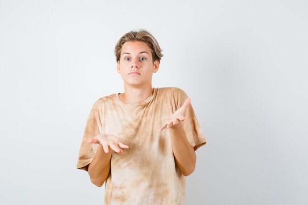 Portrait of cute teen boy showing helpless gesture in t-shirt and looking puzzled front view