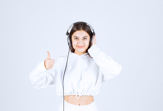 Portrait of a cute young girl model with headphones showing a thumb up .