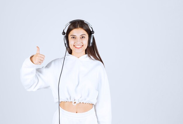 Portrait of a cute young girl model with headphones showing a thumb up .