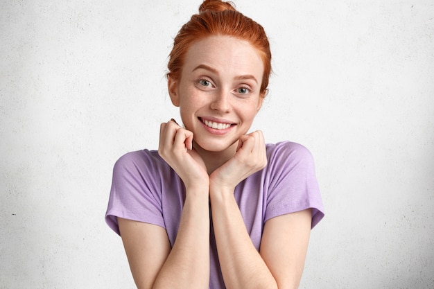 Free photo portrait of delighted lovely red haired woman with freckled skin, smiles happily at camera, satisfied with new purchases, dressed casually