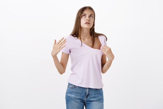 Portrait of displeased cute european woman suffering from hot summer pulling t-shirt and making wind with palm to cool while walking under sun looking up irritated