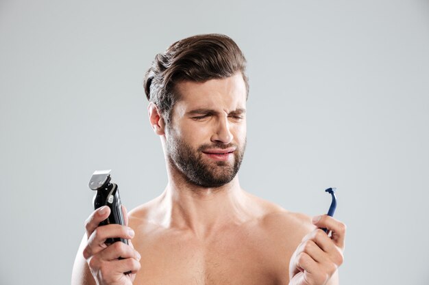 Portrait of a doubtful young man choosing razor