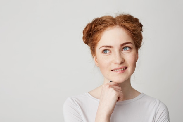 Portrait of dreamy young pretty ginger girl thinking dreaming touching chin smiling biting lip .