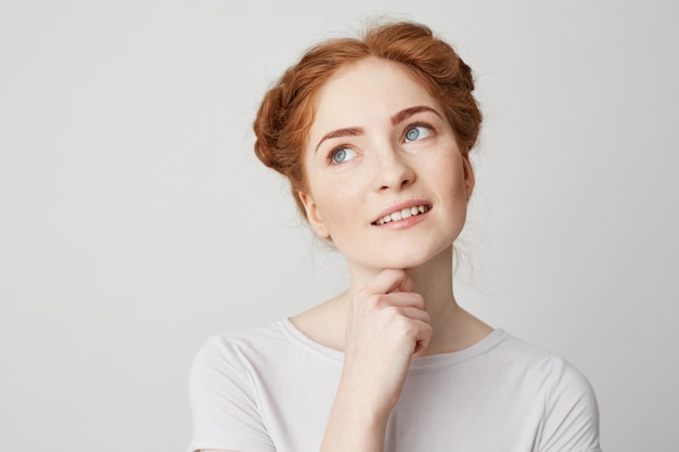 Free photo portrait of dreamy young pretty girl with red hair thinking dreaming touching chin .