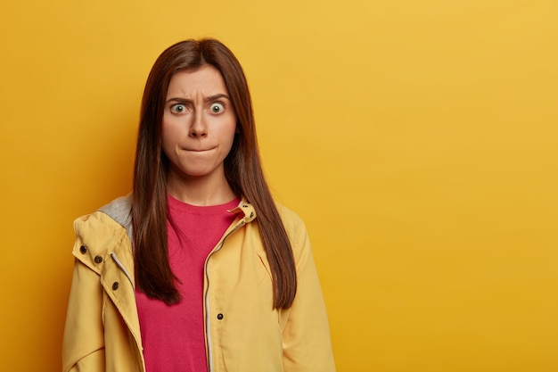 Free photo portrait of emotional worried european woman presses lips, tries to control her emotions, raises eyebrows, wears pink jumper and anorak