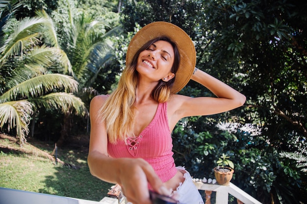 Portrait of european fit slim pretty woman without make up, natural light, with long hair, pink summer top and straw hat