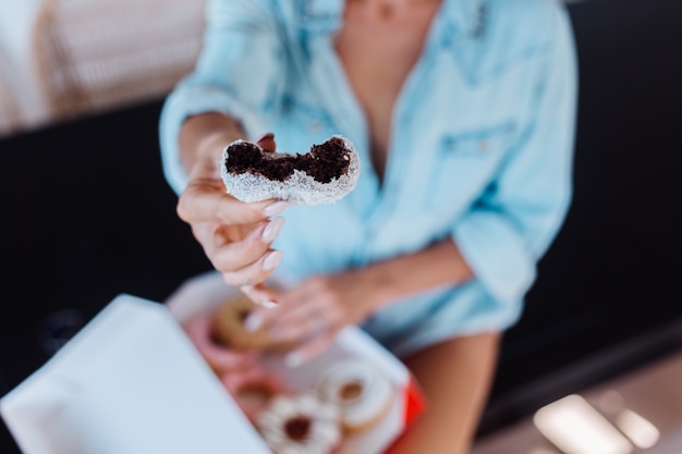 Free photo portrait of european woman with blonde hair enjoying donuts in kitchen at home villa.