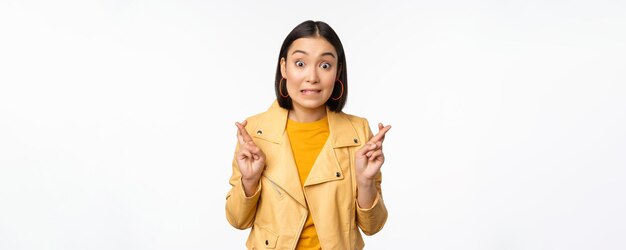 Portrait of excited asian woman looks hopeful wishing praying or begging waiting for news standing over white background smiling enthusiastic