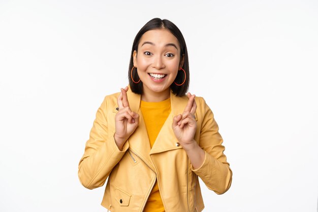 Portrait of excited asian woman looks hopeful wishing praying or begging waiting for news standing over white background smiling enthusiastic