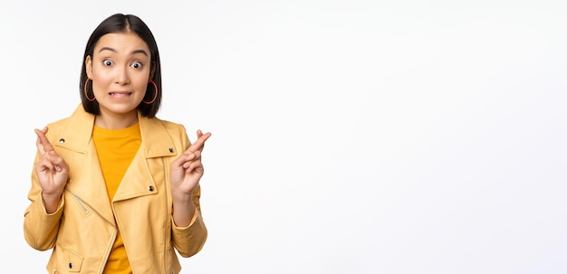 Portrait of excited asian woman looks hopeful wishing praying or begging waiting for news standing over white background smiling enthusiastic