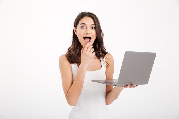 Portrait of an excited woman dressed in tank-top using laptop