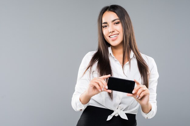 Portrait of an excited young business woman pointing blank screen mobile phone isolated on white